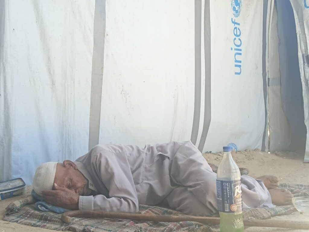 Jumaa Abu Khatla resting on a rug inside a UNICEF tent in Gaza, with a walking stick and water bottle beside him.
